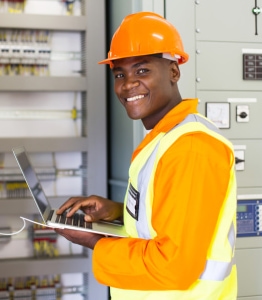 Male technician wearing a hard hat and safety vest working on a computer